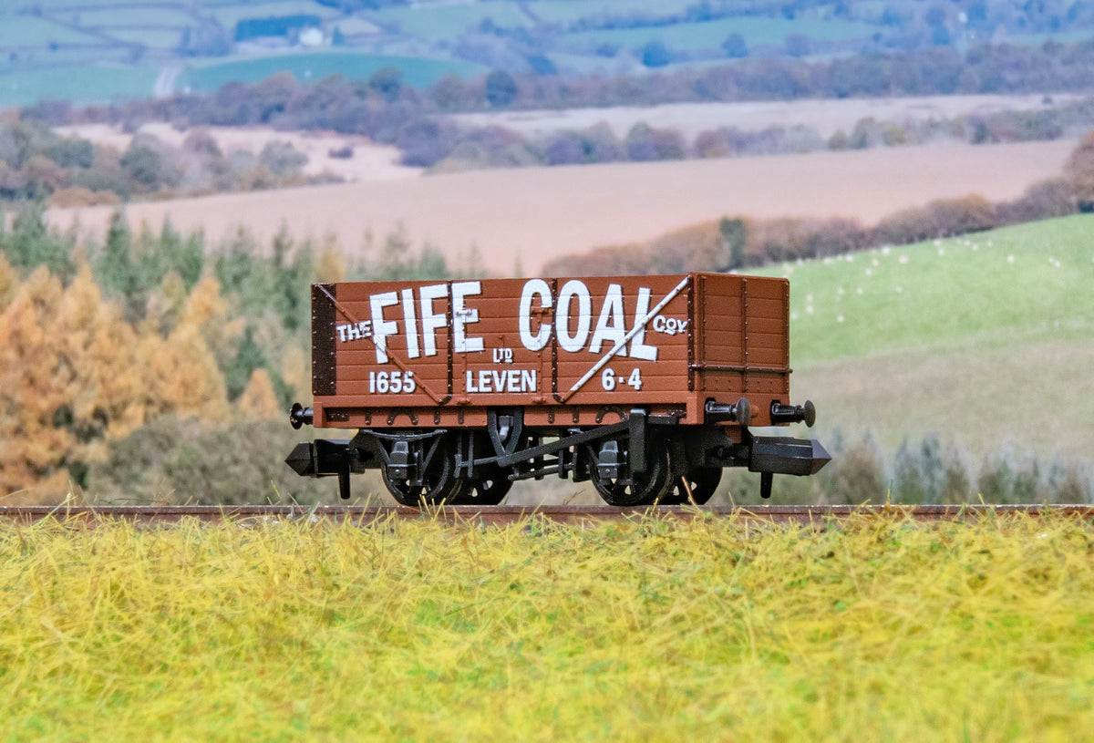 A miniature model of a vintage brown coal wagon with white lettering reading 'THE FIFE COAL COY' and '1655 LEVEN 6-4' sits on a model railway track with a blurred rural landscape background.